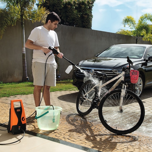 BLACKDECKER PW1450TD pressure washer used outdoors to clean a white bicycle near a black car.