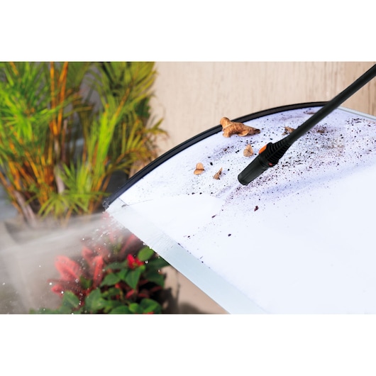 BLACKDECKER PW1450TD pressure washer nozzle cleaning dirt and leaves from a glass surface outdoors.