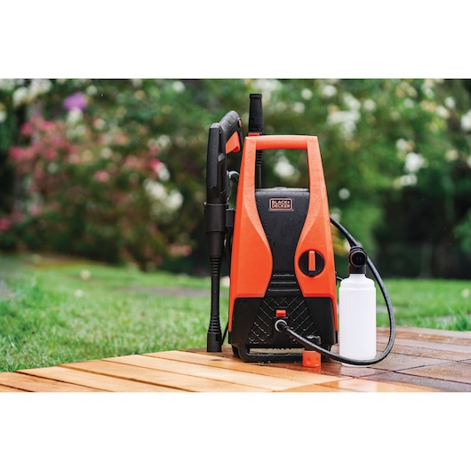 BLACKDECKER PW1450TD pressure washer with orange and black body, detergent bottle, and spray gun on patio.