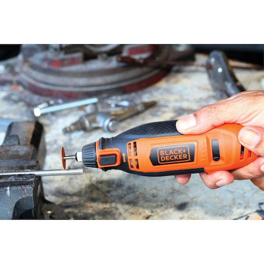 BLACK+DECKER RT18KA rotary tool in hand, orange and black design, used for grinding metal on a workbench.