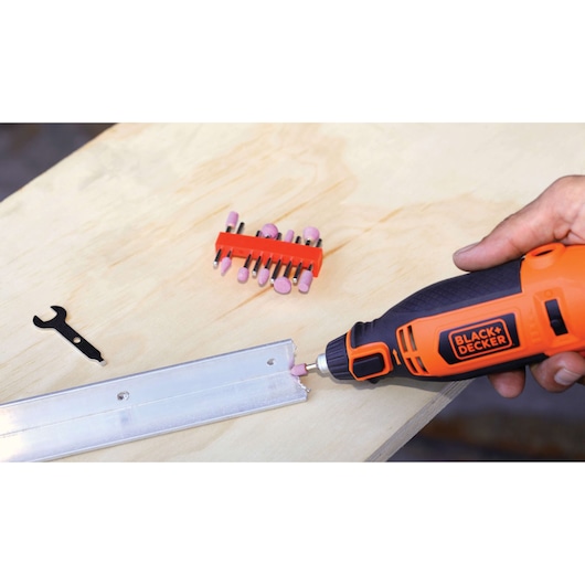 BLACK+DECKER RT18KA rotary tool, orange and black, used for grinding metal on table with attachments and wrench visible.